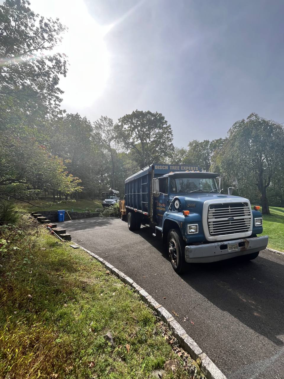 Blue Disch dump truck pulling out of a wooded driveway in fall